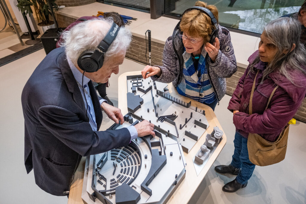 Twee slechtzienden verkennen de maquette met hun handen en luisteren naar de audio