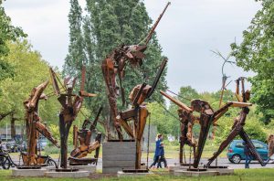 Beelden van menselijke vomen van hout. Naast houd zijn er schroeven, bouten en kettingen in de beelden verwerkt.