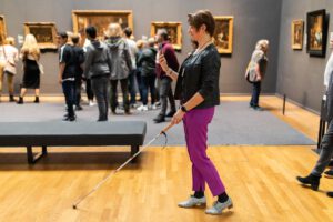 Blinde vrouw navigeert door Rijksmuseum met taststok en een smarthphone