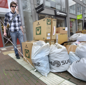 Blinden man met geleide stok volgt geleide lijn en loopt op tegen dozen en vuilnis.