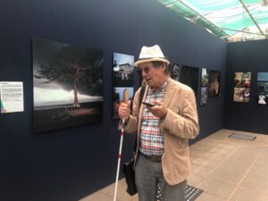 Hannes Wallrafen staat centraal in beeld en kijkt naar zijn smartphone. Op de achtergrond zijn de foto's van zijn expositie te zien.