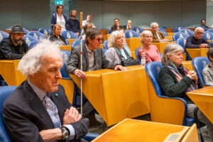 Blinden en slechtzienden zitten in de banken van de plenaire zaal.