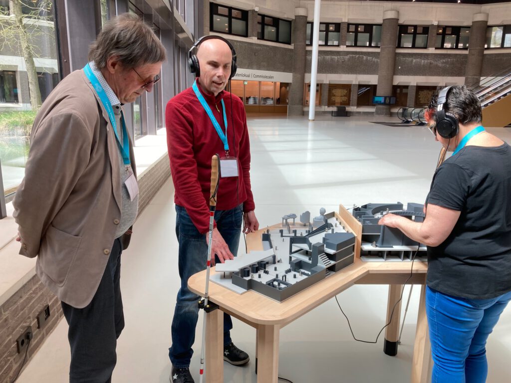 Blinde man verkent de maquette met zijn handen en beluistert door een koptelefoon de uitleg