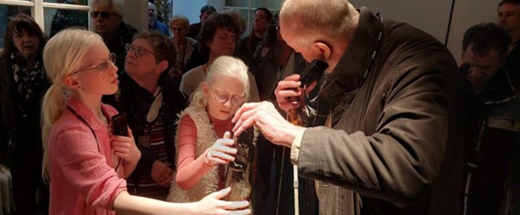 Een man met een taststok luistert naar de audiotour 